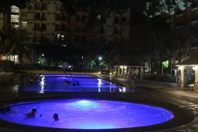 a large blue pool with people in it at night at CHATEAU ELYSEE A10 near airport in Manila