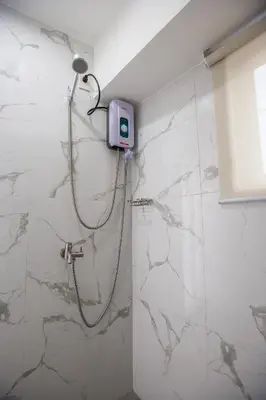 a shower in a bathroom with white marble walls at Circuit Hostel in Manila