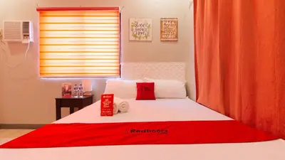 a bed with red and white pillows and a window at RedDoorz near Christ the King Medical Center in Manila