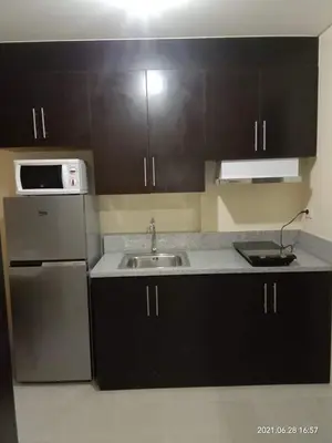 a kitchen with black cabinets and a sink and a refrigerator at The Rochester Condo in Manila