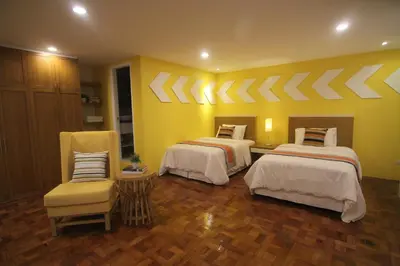 a yellow room with two beds and a chair at Bryan Condo Suites Makati near Airport in Manila