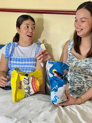 a woman and a girl sitting on a bed with chips at airobedz MANILA - A Value Hotel in Manila