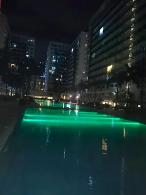a pool with green lights in a city at night at Moa's Spot at Sea Residences in Manila