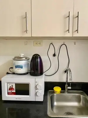 a kitchen counter with a sink and a microwave at Azenith Staycation At Sea Residences Moa in Manila