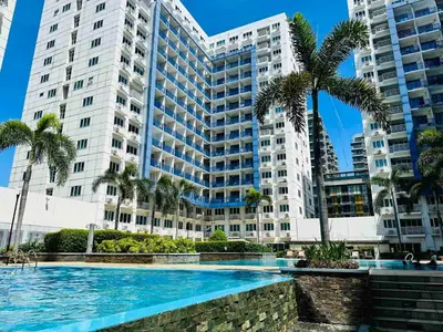 a large building with palm trees and a swimming pool at Sea Residences - Tino Val in Manila