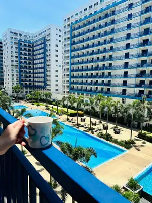 a person holding a coffee cup on a balcony overlooking a pool at Sea Residences in Manila