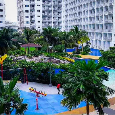 a resort with a playground and a pool with palm trees at Sabina's one bedroom condo at Shore tower C in Manila