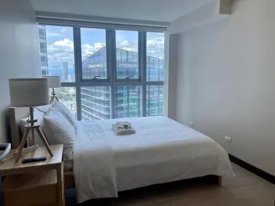 a bedroom with a white bed and a large window at Bright 2-bedroom condo with pool in BGC Uptown in Manila