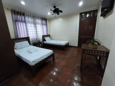 a room with two beds and a chair and a table at Makabata Guesthouse & Cafe in Manila
