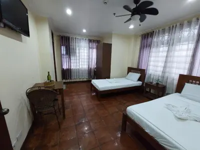 a room with two beds and a table and a tv at Makabata Guesthouse & Cafe in Manila