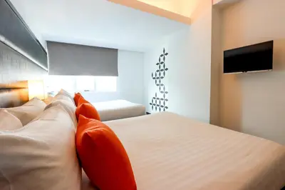 a bedroom with a bed with orange pillows and a tv at Privato Ortigas in Manila