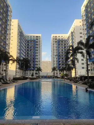 a large swimming pool with palm trees and buildings at Bliss Staycation at Sea Residences by John in Manila