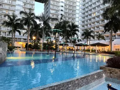 a large swimming pool with palm trees and buildings at Amour Staycation Shell residences in Manila