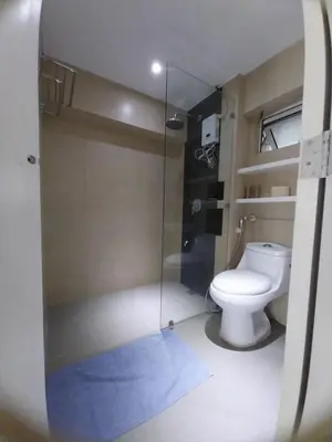 a bathroom with a toilet and a glass shower at 2 BR loft-type condo Fort Victoria in Manila