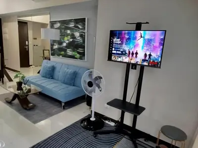 a living room with a blue couch and a flat screen tv at Cozy 1BR UPTOWN PARKSUITES Tower1 BGC in Manila