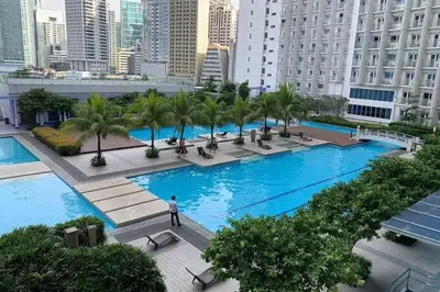 a large pool with palm trees in a city at Netflix, Destina Stays at Jazz Residences Makati, MetroManila in Manila
