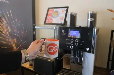 a person holding a coffee cup in front of a coffee machine at Go Hotels Plus Mandaluyong in Manila