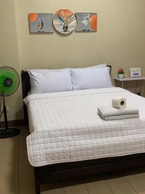 a bed with a white comforter and a alarm clock on it at MRMCONDOTEL cluster 1 2H in Manila