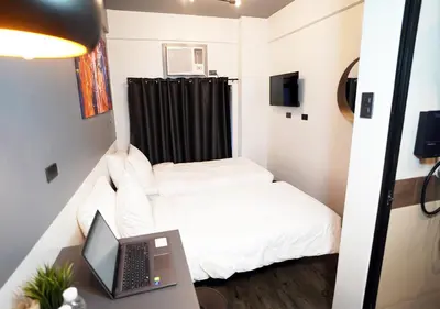 a small room with a bed and a laptop on a desk at mySTAY Hotel BGC West in Manila