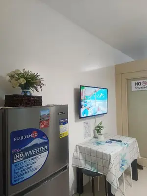 a kitchen with a refrigerator and a table and a tv at Amigo's Place at Sea Residences in Manila