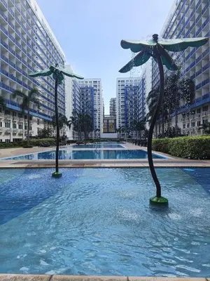 a pool with two umbrellas in the water with buildings at Amigo's Place at Sea Residences in Manila