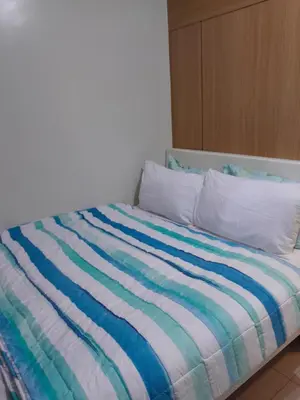 a bed with a blue and white striped comforter at Jamaica's Place 1br Amenities View at Shell Residences in Manila