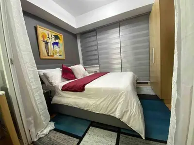 a small bedroom with a bed with white sheets and red pillows at Cozy 1BR cityview with Balcony and near Airport in Manila