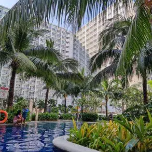a swimming pool with palm trees in front of a building at Shore 1 Residences Staycation By Ms Chona in Manila