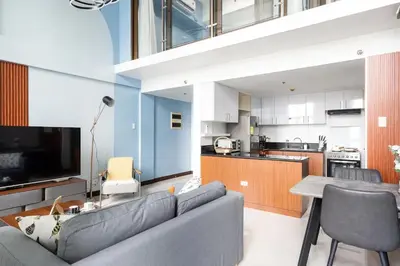a living room with a couch and a kitchen at Stylish loft, 65 in UHDTV w Fast WiFi + Pool & Gym in Manila