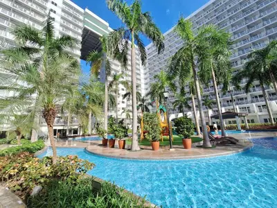 a resort pool with palm trees and buildings at Best staycation at Shell residences in MOA complex in Manila