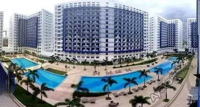 a large building with a large swimming pool with palm trees at Sea Residences Staycation by TVANS CONDOTEL Pasay City in Manila