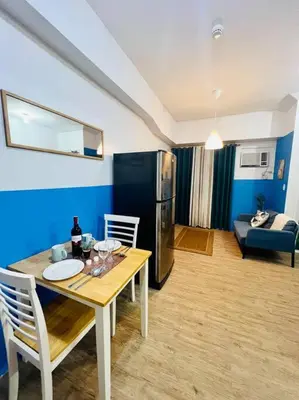 a living room with a table and a refrigerator at Cozy Place Anuva Residences in Manila