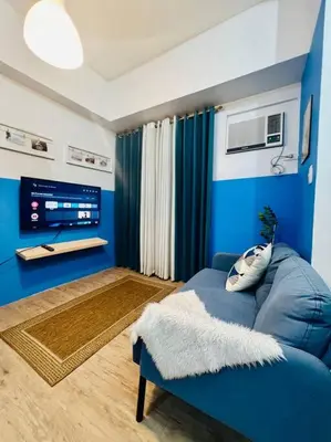 a living room with a blue couch and a tv at Cozy Place Anuva Residences in Manila