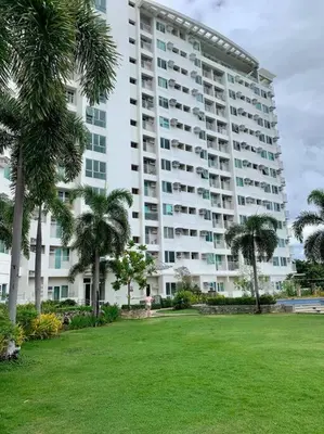 a large building with palm trees in front of a park at Cozy Place Anuva Residences in Manila