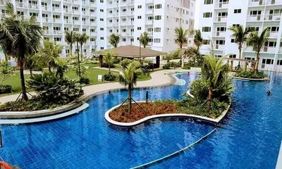 a large blue swimming pool with palm trees and a building at Shore Residences MOA Staycation in Manila