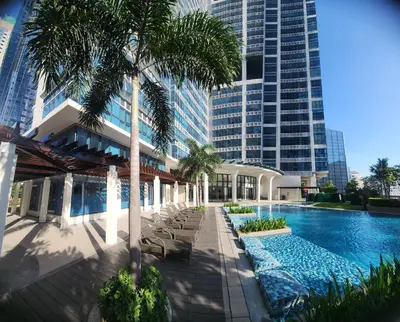 a swimming pool with palm trees and a building at 8U Pristine & Cozy Stay at Uptown Mall BGC across Mitsukoshi with FREE Parking and Balcony in Manila