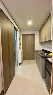 a kitchen with wooden cabinets and a sink and a door at Cozy 1Br with Netflix & Balcony Pool View Condo in Manila