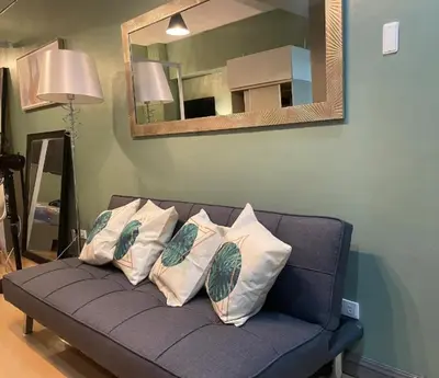 a blue couch with four pillows and a mirror at Poolview Family Room Greenbelt Makati in Manila