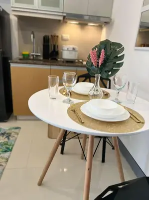 a table with plates and glasses and a vase with flowers at Cozy Studio Viceroy Residences McKinley Hill Bgc in Manila