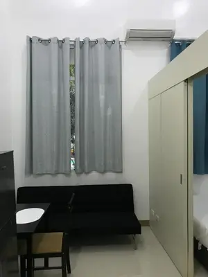 a living room with a black couch and a window at South Residences staycation in Manila