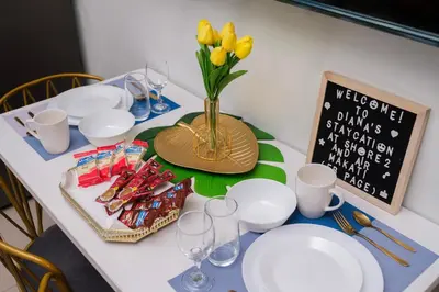 a table with white plates and a vase with yellow flowers at 2 Side-by-Side P00L Front Condos, 6 Beds, 2 CR, 2 Kitchen at MOA in Manila