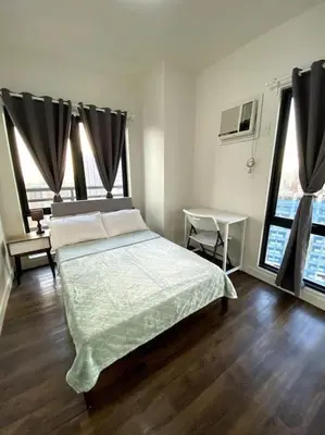 a bedroom with a bed and a table and two windows at Modern Condo Apt in Flair Tower South, Mandaluyong in Manila