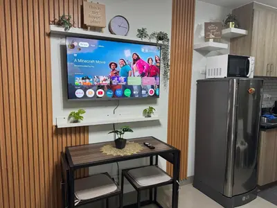 a television on a wall with a table and a refrigerator at Shore 2 Condo unit near MOA in Manila