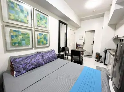 a bedroom with a bed with purple pillows and a desk at KL Tower Makati near AIM, Greenbelt 90mbps WIFI in Manila