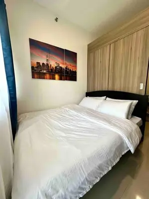 a bedroom with a white bed with a painting on the wall at Modern 1-BR Condo Unit in Manila